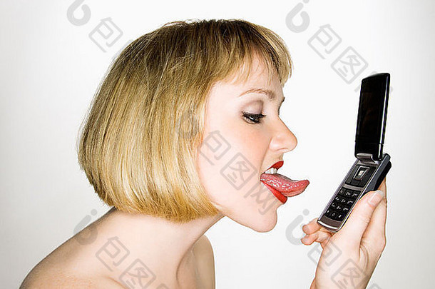 一位年轻的金发白种女人的侧视图，她正准备舔她的手机