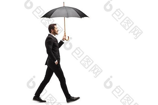 一个英俊的商人拿着一把开着的伞走在白色背景上的全长侧面照