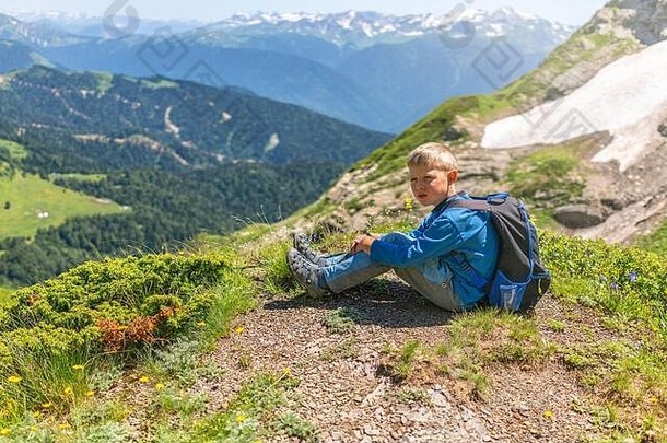 夏天，一个男孩带着<strong>登山杖</strong>和背包在一座积雪的山顶上休息。山顶在夏天。高加索，俄罗斯