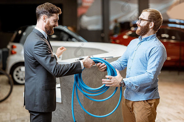 销售员将电动车充电电缆交给汽车经销商的客户。买电动车的男人