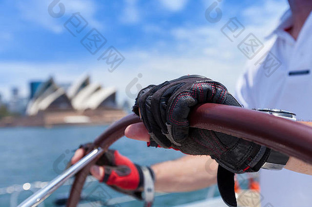 在一个阳光明媚的日子里，在悉尼港歌剧院附近航行。船长在游艇上握住方向盘的特写镜头
