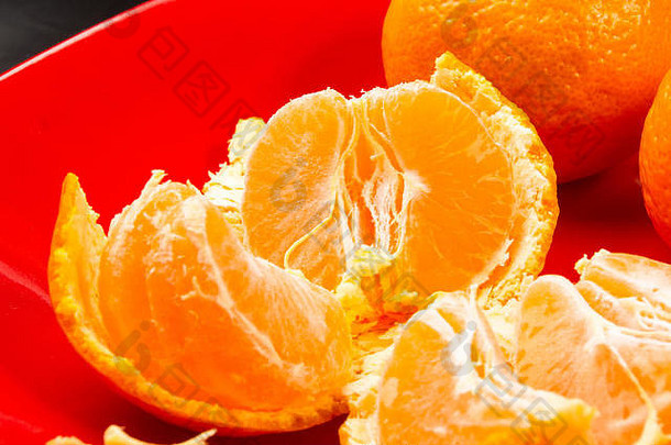 橘子，去皮的橘子和橘子片在黑色背景上的红色盘子里