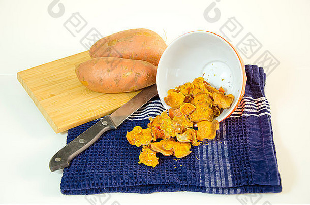 一碗的烤红薯片倒在厨房毛巾、刀和切菜板上的生蔬菜上。健康的