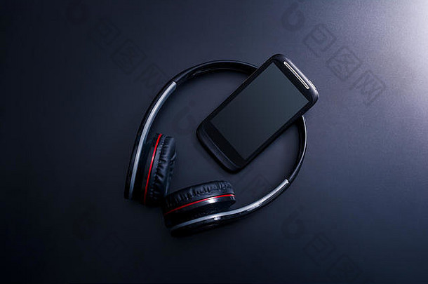 黑色智能手机靠在黑色头戴式耳机上，背景为黑色，带有反光
