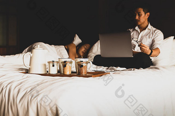 当他的妻子在<strong>床</strong>上睡觉时，这位商人正在用笔记本电脑工作。
