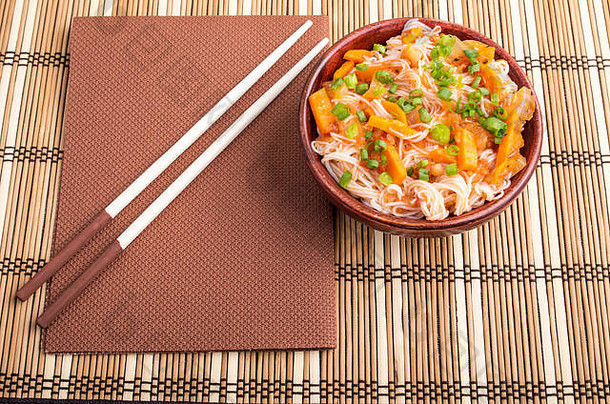 亚洲菜肴的俯视图，米粉和蔬菜调味品放在一个带条纹的垫子上的小木碗中