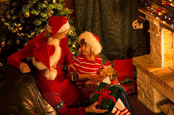 一家人戴着红帽，拿着礼物坐在壁炉旁的圣诞树旁
