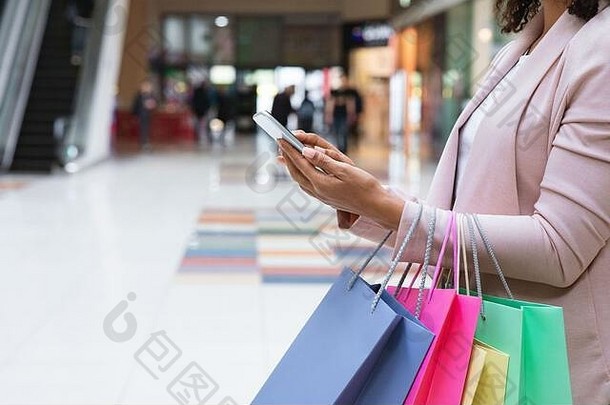 现金返还奖金。购物后带购物袋在商场使用智能手机的女士