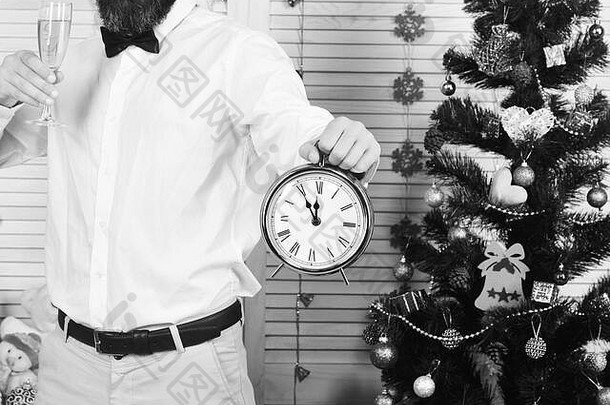 聚会，派对男人。时钟显示午夜的家伙圣诞节树木墙背景庆祝活动一年时间概念男人。胡子持有玻璃香槟报警时钟