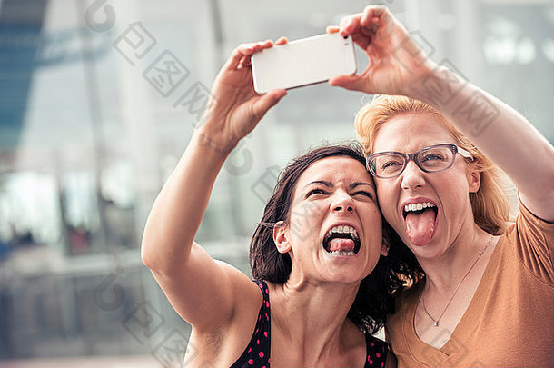 两个女人在城市街道上用智能手机自拍。
