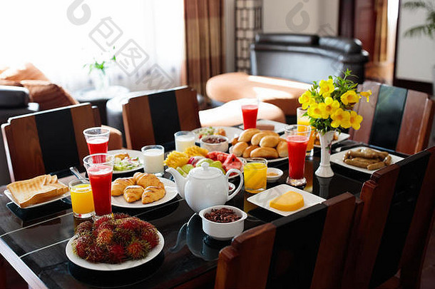 黑木桌上有面包和香肠的健康早餐。家庭早餐热带水果、鲜榨果汁、吐司和牛角面包