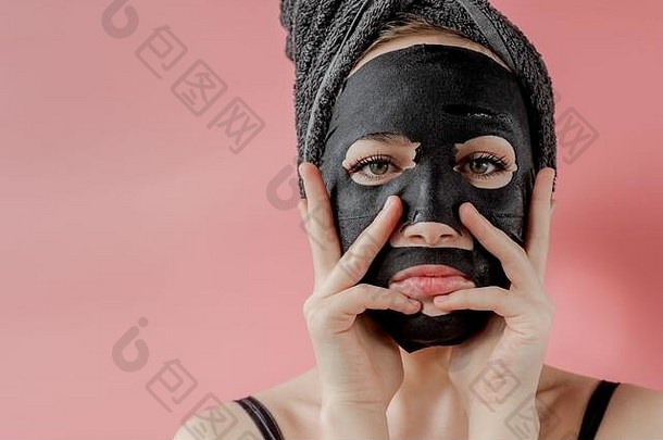 年轻女子在粉色背景下涂黑色化妆面料面膜。木炭去皮面膜、spa美容、护肤、美容