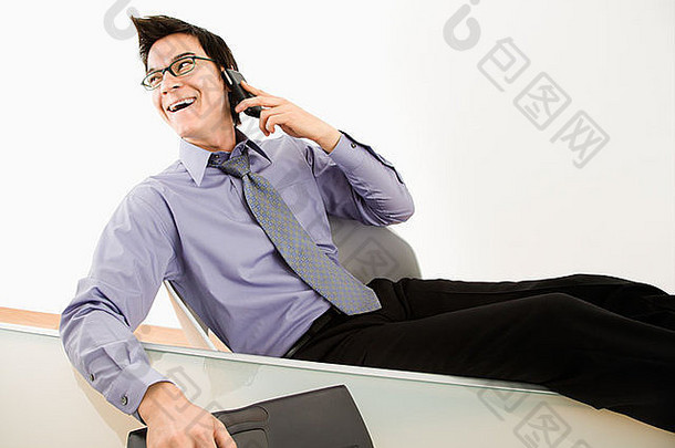 笑亚洲商人坐着桌子上会说话的手机