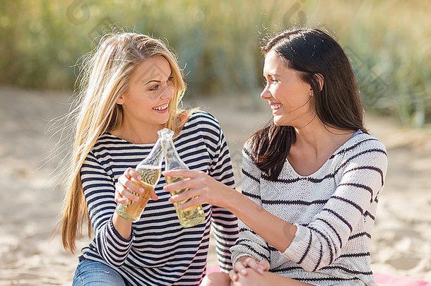快乐的年轻女子在海滩上喝啤酒