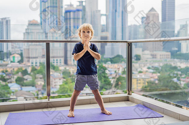 快乐的小男孩正在阳台上练习瑜伽，可以看到大城市的全景