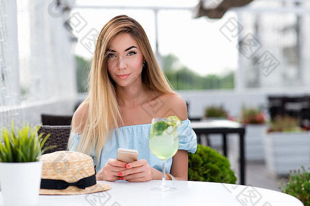 美丽的女孩长头发女人夏天咖啡馆餐厅坐在表格蓝色的衣服特写镜头手电话表格玻璃鸡尾酒