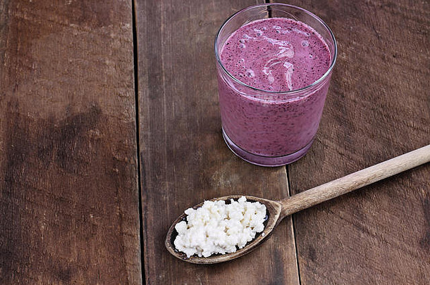 木勺中的开菲尔谷物放在蓝莓开菲尔冰沙前。凯菲尔是提供强力益生菌的顶级健康食品之一。