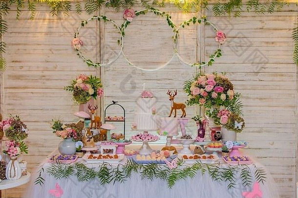 豪华的糖果和生日蛋糕桌上装饰着插花和精致的野生动物，背景是轻质木板。博