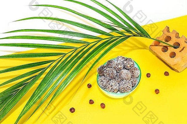蛋白质花生酱能量片或能量球。生巧克力松露，盘上有坚果，黄色背景为棕榈叶。