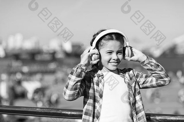 女孩在户外用现代耳机听音乐。小女孩戴着耳机听歌曲。音乐帐户播放列表。定制您的音乐。发现新的音乐风格是进入文化的好方法。
