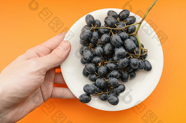 橙色背景的盘子里的黑葡萄。