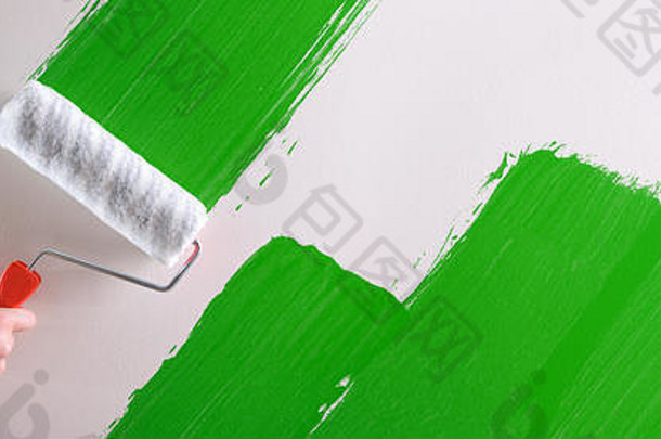 男子用滚筒在白墙上手工画出绿色样品。水平构图。