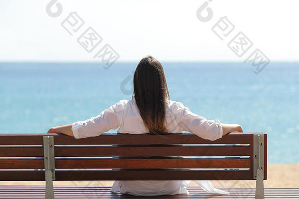 坐在长椅上看大海的快乐女人的后视图肖像