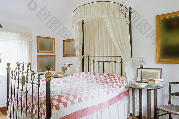 古董黄铜床上带白色百叶窗帘的金属天篷，乡村卧室内有粉色 白色被子，带木制床头柜
