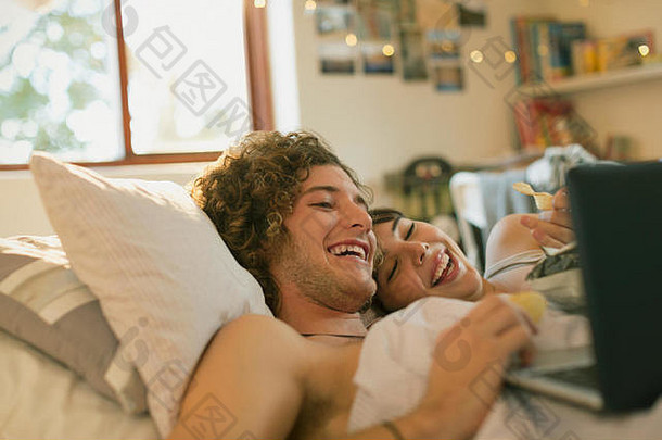 微笑年轻的夫妇铺设床上移动PC