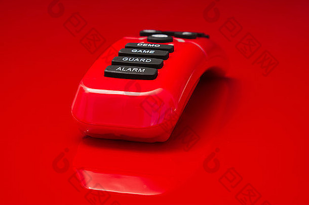 红色反光的遥控器躺在红色的镜面上，按钮上印有警报、警卫、游戏和演示