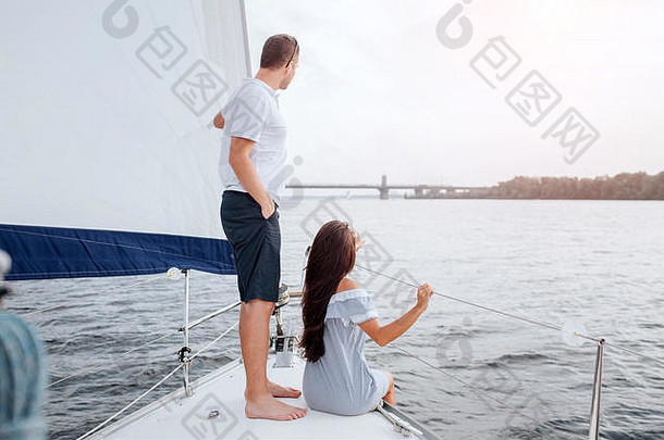 美丽的夫妇游艇弓向前年轻的女人坐着男人。站手口袋里管