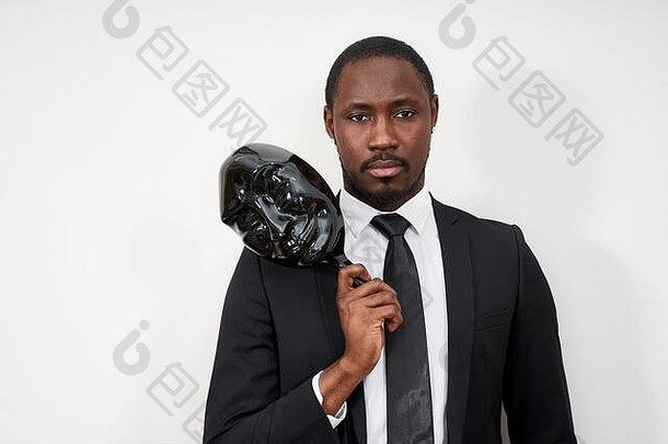 身穿黑色西装的非洲年轻人摘下塑料面具露出脸