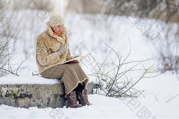 女人坐着板凳上阅读书冬天雪