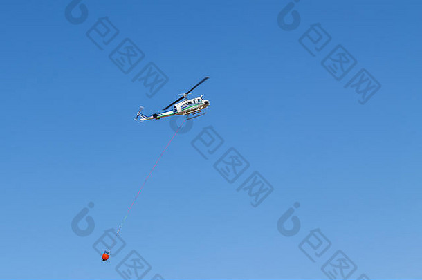空中灭火<strong>直升机</strong>，带红色水桶，对抗蓝天。