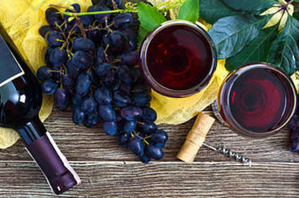 木桌上放着红酒、酒瓶、开瓶器、蓝葡萄、树叶的酒杯。葡萄酒背景与空间。俯视图，平面布置。横幅