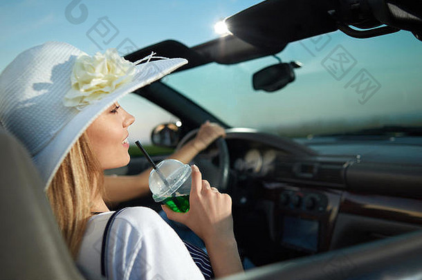 漂亮的金发模特坐在司机旁<strong>边</strong>的敞篷车里，看着远处。迷人的年轻女子拿着柠檬水杯，面带微笑。戴着带花的<strong>白边</strong>宽<strong>边</strong>帽的女孩。
