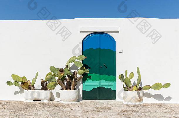 绿色和蓝色手绘<strong>门</strong>和仙人掌植物，白色墙壁是意大利阿普利亚奥斯<strong>图</strong>尼小村庄典<strong>型</strong>的房屋。