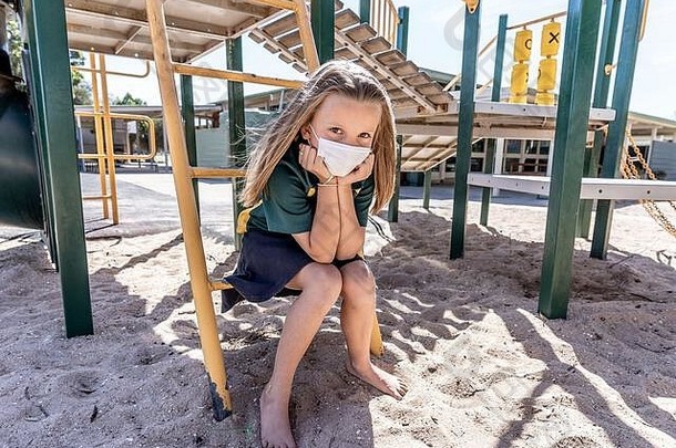 2019冠状病毒疾病爆发学校关闭。当学校关闭时，戴着面具的悲伤女生在空旷的操场上感到沮丧和孤独。限制