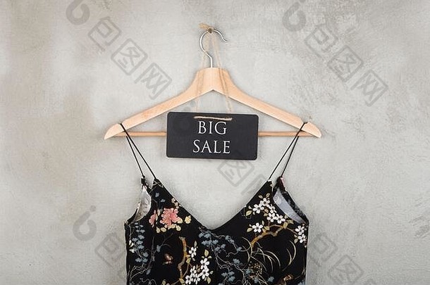 购物折扣概念-黑板上有文字“大减价”，挂在灰色背景的衣架上有美丽的黑色小连衣裙，上面有花卉图案