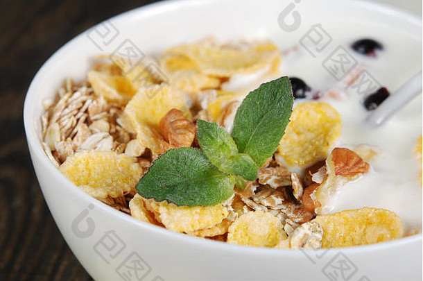 燕麦、小麦和玉米片，配坚果、酸奶和薄荷叶，装在黑色木质背景上的白色小碗中