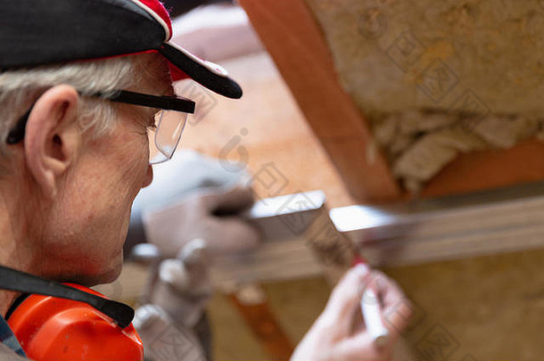 戴谷歌眼镜的人在未完工的阁楼天花板上的金属框架上做了一个标记。阁楼保温与装修