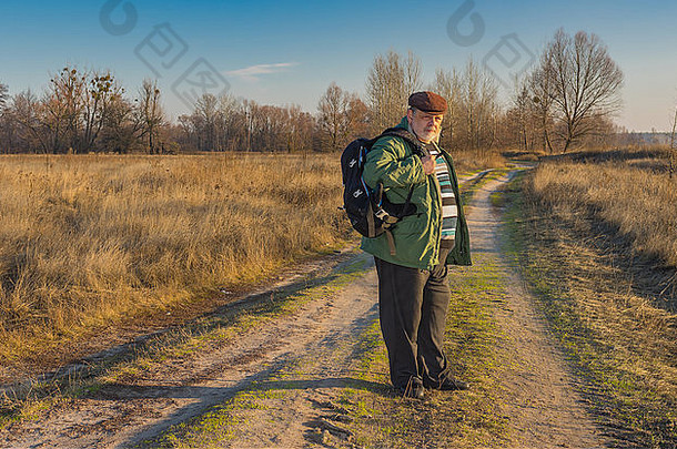 秋天的傍晚，背着背包站在乡间小路上的高级徒步旅行者