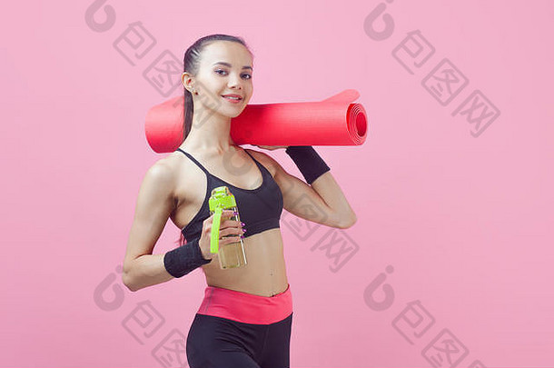 一位迷人的运动型浅肤色女孩的肖像，可爱，穿着紧身运动服，一只手拿着粉色<strong>瑜伽</strong>垫和一个运动用瓶子。