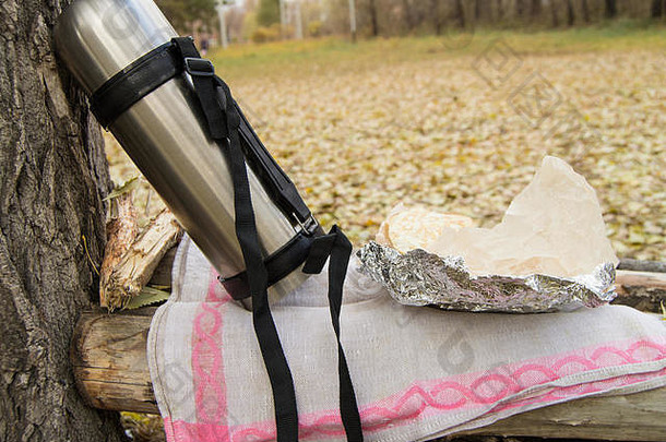 秋天在公园野餐时，一大瓶热茶、咖啡和包裹在锡箔纸三明治里