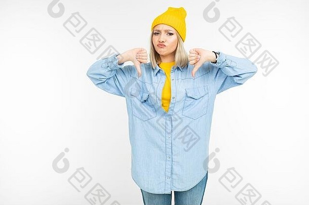 穿着时尚牛仔衬衫、头戴黄色帽子的心疼可爱女孩在白色摄影棚背景下表现出厌恶