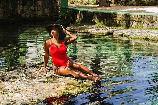 年龄在25岁至30岁之间的黑人妇女，穿着红色比基尼，享受着天然水源的<strong>清新</strong>，<strong>周</strong>围是热带自然