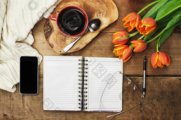 头顶上，一束打开的书、手机、咖啡和鲜花放在一张木质桌面上，准备制定日程。平放俯视图样式。