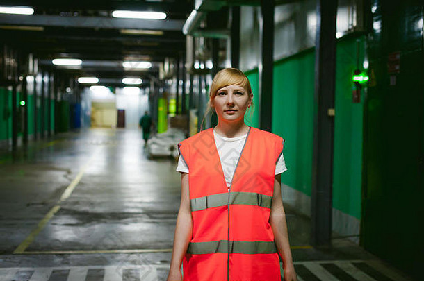 一名穿着橙色长袍背心的女员工在<strong>生产</strong>设施的工作空间内，对仓库<strong>生产</strong>区域进行控制