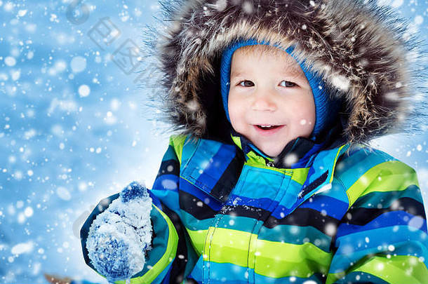 下雪时，戴着针织帽子、手套和围巾的男孩在户外玩耍