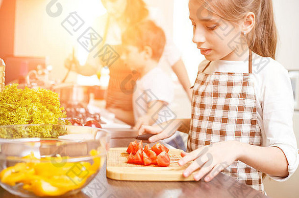 一个十几岁的小女孩和她的家人一起在<strong>厨房</strong>做饭。可爱的女孩切西红柿做沙拉
